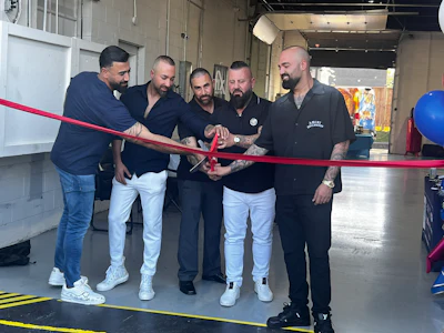 Five men cutting a red ribbon at a business opening or launch event