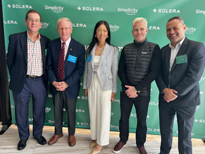 Five professionals posing at Solera corporate event with branded green backdrop