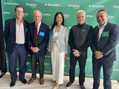 Five professionals posing at Solera corporate event with branded green backdrop