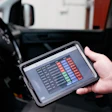 Hand holding tablet displaying data metrics inside a vehicle dashboard