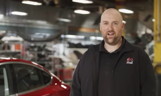 Bald man in black jacket standing in automotive manufacturing facility