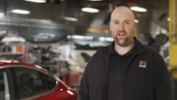 Bald man in black jacket standing in automotive manufacturing facility