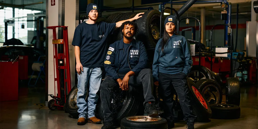 Three automotive workers in navy uniforms standing near tires in workshop