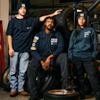 Three automotive workers in navy uniforms standing near tires in workshop
