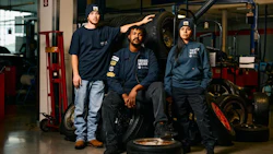Three automotive workers in navy uniforms standing near tires in workshop