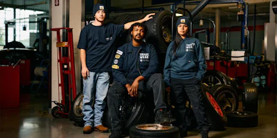 Three automotive workers in navy uniforms standing near tires in workshop
