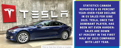 Tesla electric vehicle in dark blue, parked against concrete wall with Tesla logo