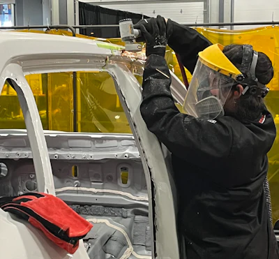 Worker in protective gear welding vehicle door frame in manufacturing facility