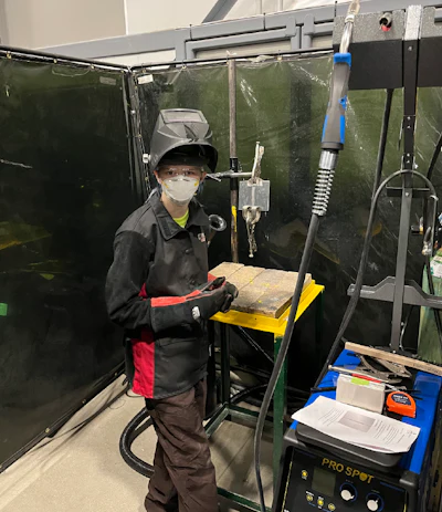 Worker in safety gear operating machinery behind protective welding screen