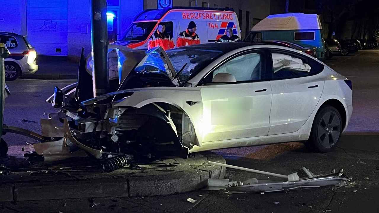 Wrecked white Tesla car at night with emergency vehicle in blue background