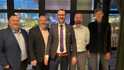 Five businessmen in professional attire standing together in modern office lobby