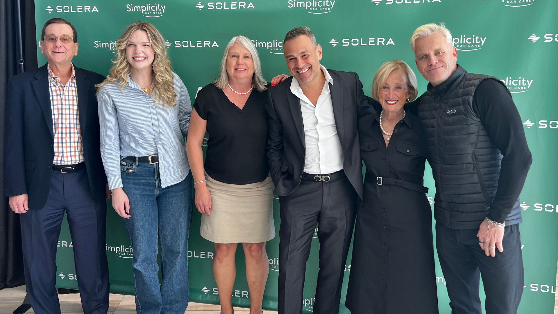 Six professionals posing in front of Solera corporate green step-and-repeat backdrop