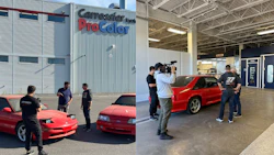 Red sports car inside auto body shop with camera crew and technicians