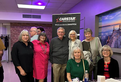 Group of six older adults posing near CarStar automotive service logo