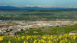 Panoramic view of mountain town with yellow wildflowers, green hills, and snow-capped peaks