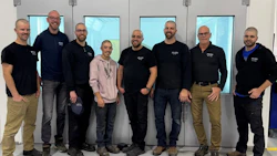 Team of seven professionals standing together in an industrial workspace