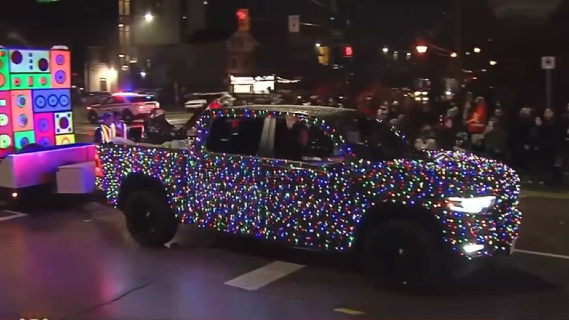 Car covered in multicolored holiday lights at night on city street