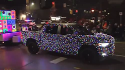 Car covered in multicolored holiday lights at night on city street