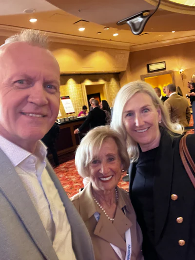 Three smiling professionals at a conference, wearing business attire