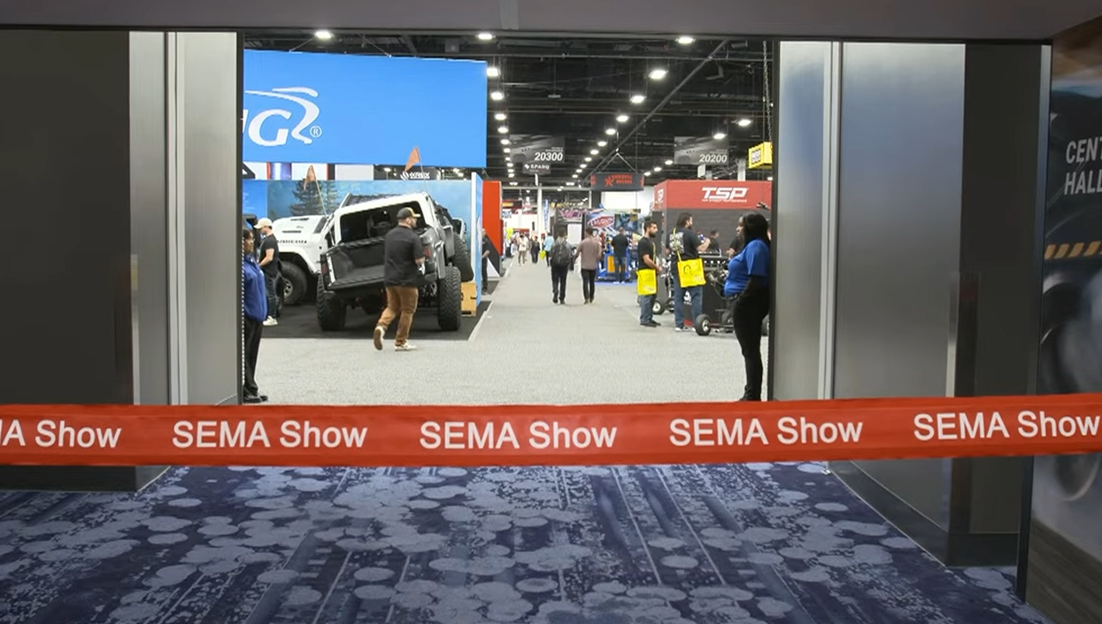 SEMA automotive trade show floor with vehicles and attendees browsing exhibits