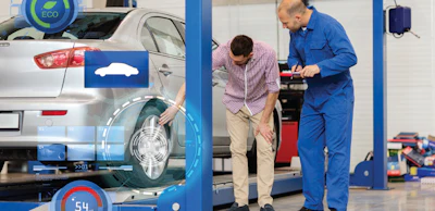 Automotive technician examining car wheel on lift in repair shop