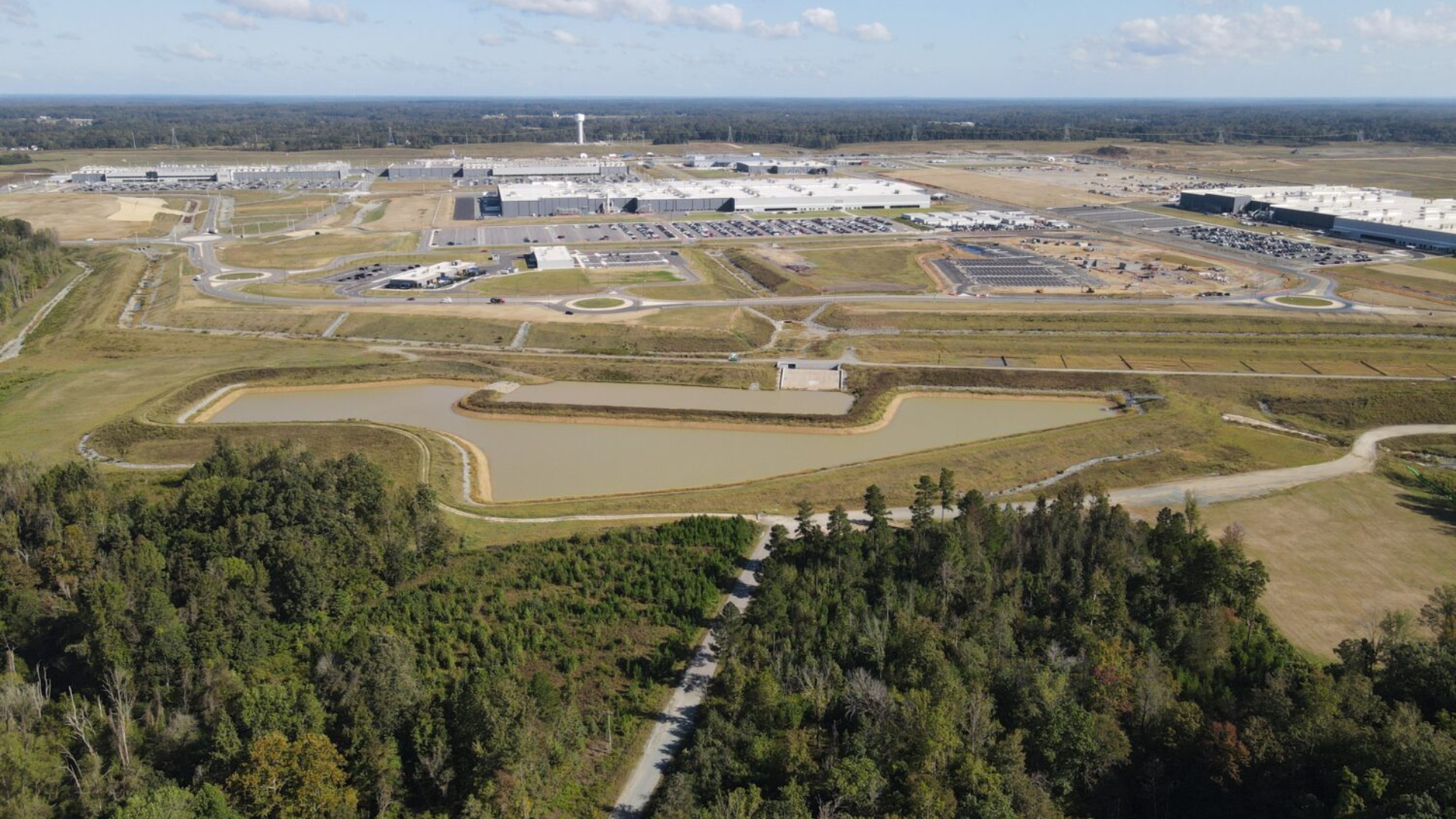 Aerial view of large industrial complex with buildings, roads, and surrounding forest landscape