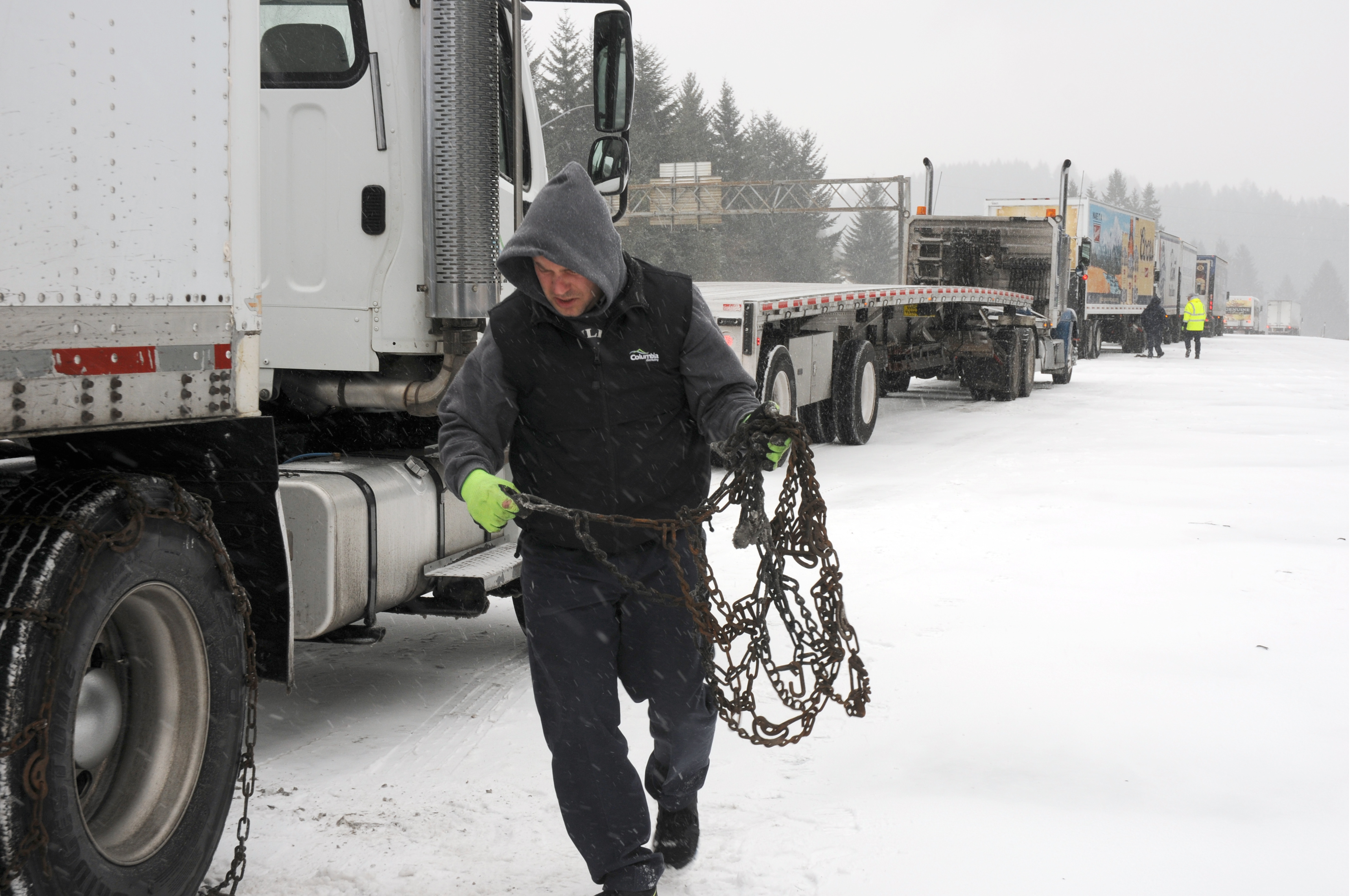 Truck driver securing snow chains on semi-truck during winter road conditions