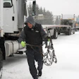 Truck driver securing snow chains on semi-truck during winter road conditions