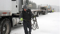 Truck driver securing snow chains on semi-truck during winter road conditions