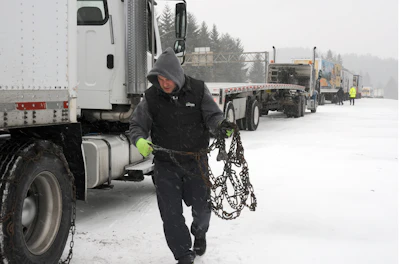 Truck driver securing snow chains on semi-truck during winter road conditions