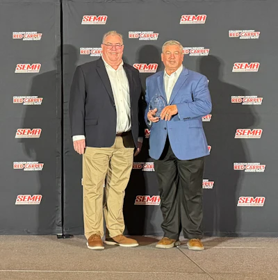 Two men at SEMA Red Carpet Awards event with organizational logos backdrop