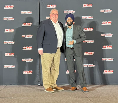 Two professionals posing at SEMA event with branded backdrop