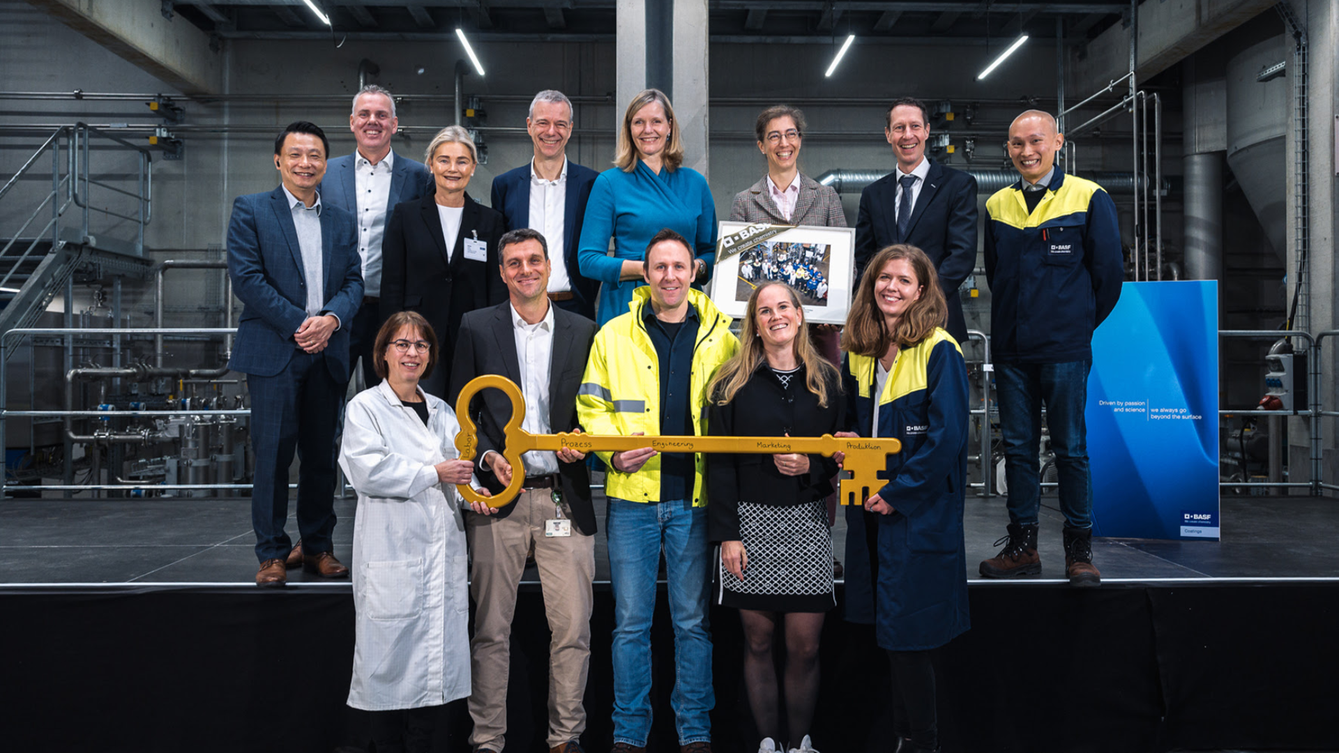 Corporate group photo with employees holding large golden key in industrial facility