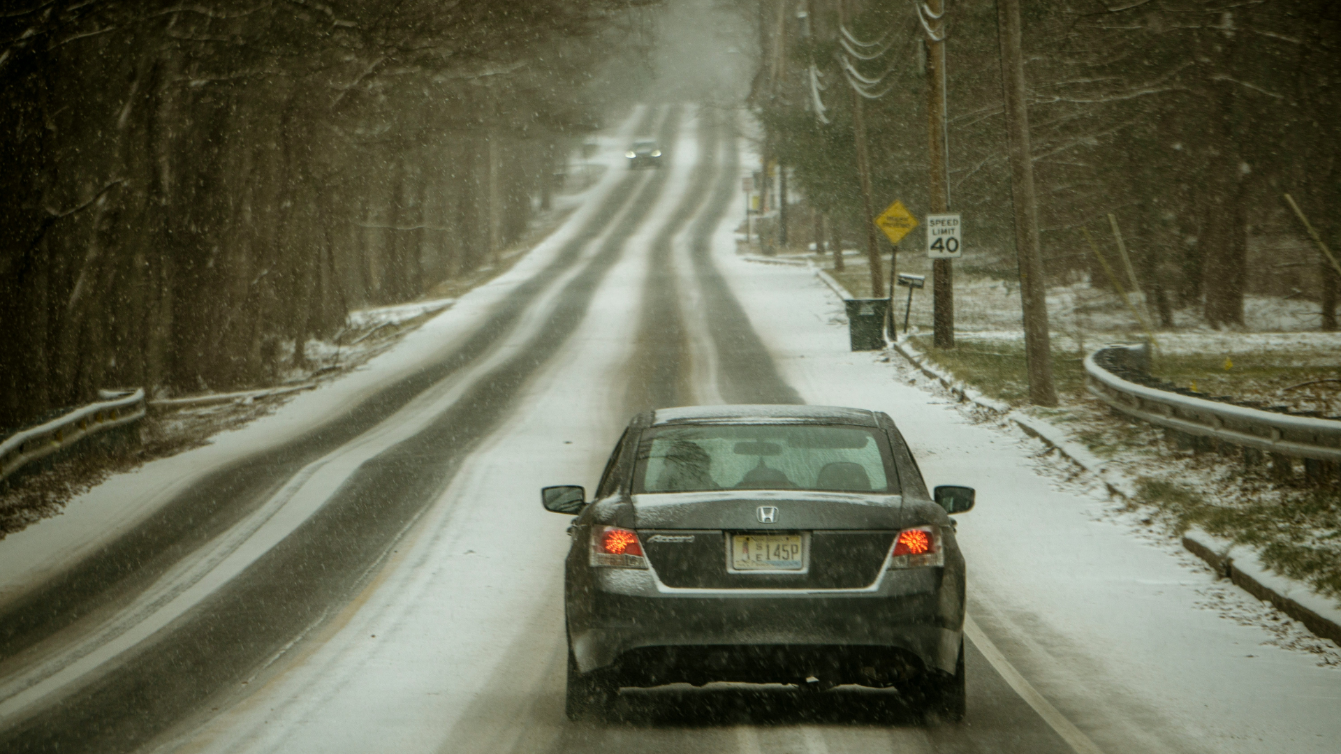 Gray Honda sedan driving on snowy, winding forest road with speed limit sign