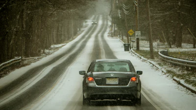 Gray Honda sedan driving on snowy, winding forest road with speed limit sign