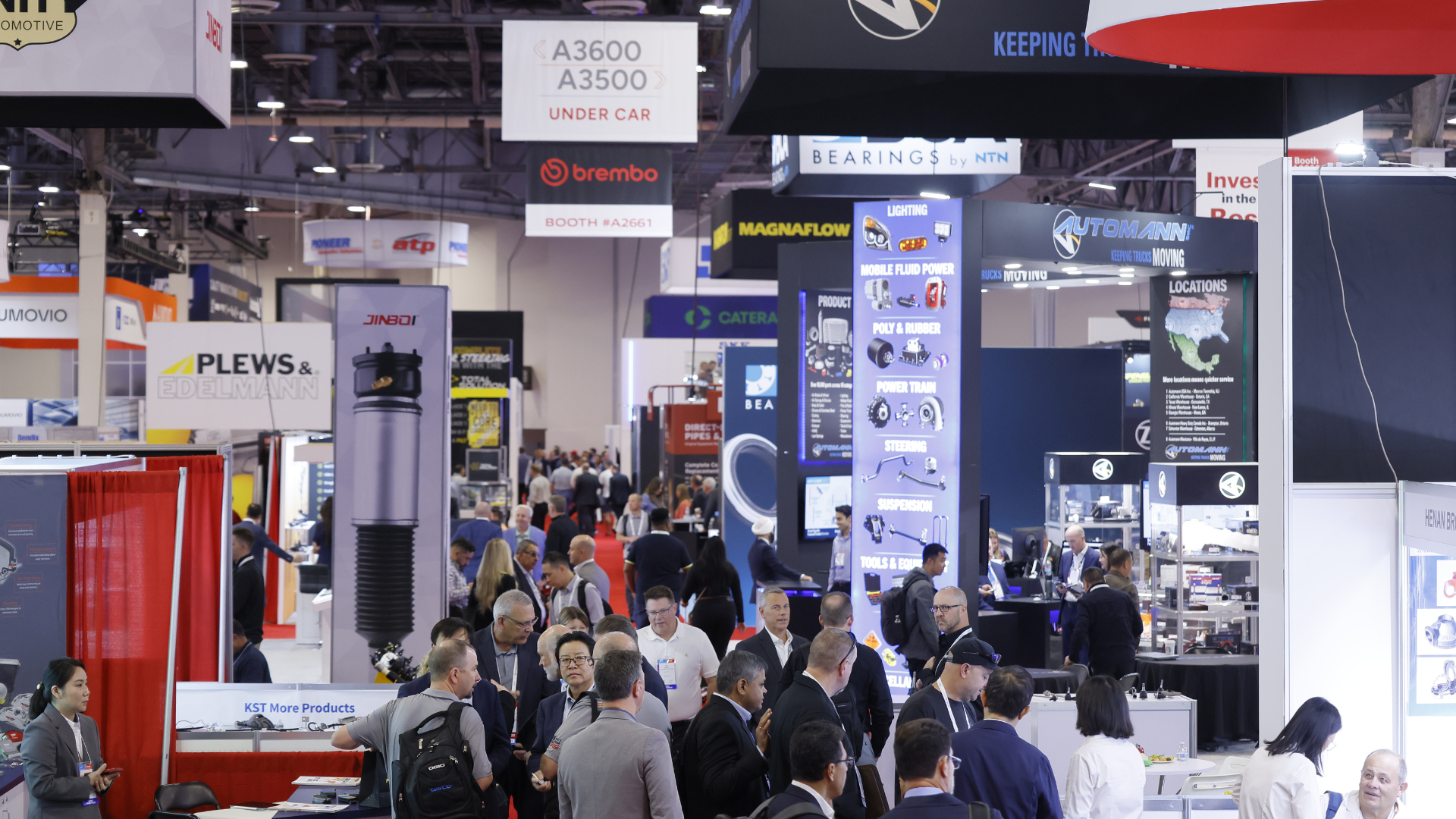 Crowded automotive industry trade show with multiple vendor booths and technical displays