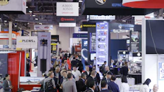 Crowded automotive industry trade show with multiple vendor booths and technical displays