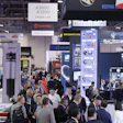 Crowded automotive industry trade show with multiple vendor booths and technical displays