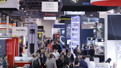 Crowded automotive industry trade show with multiple vendor booths and technical displays
