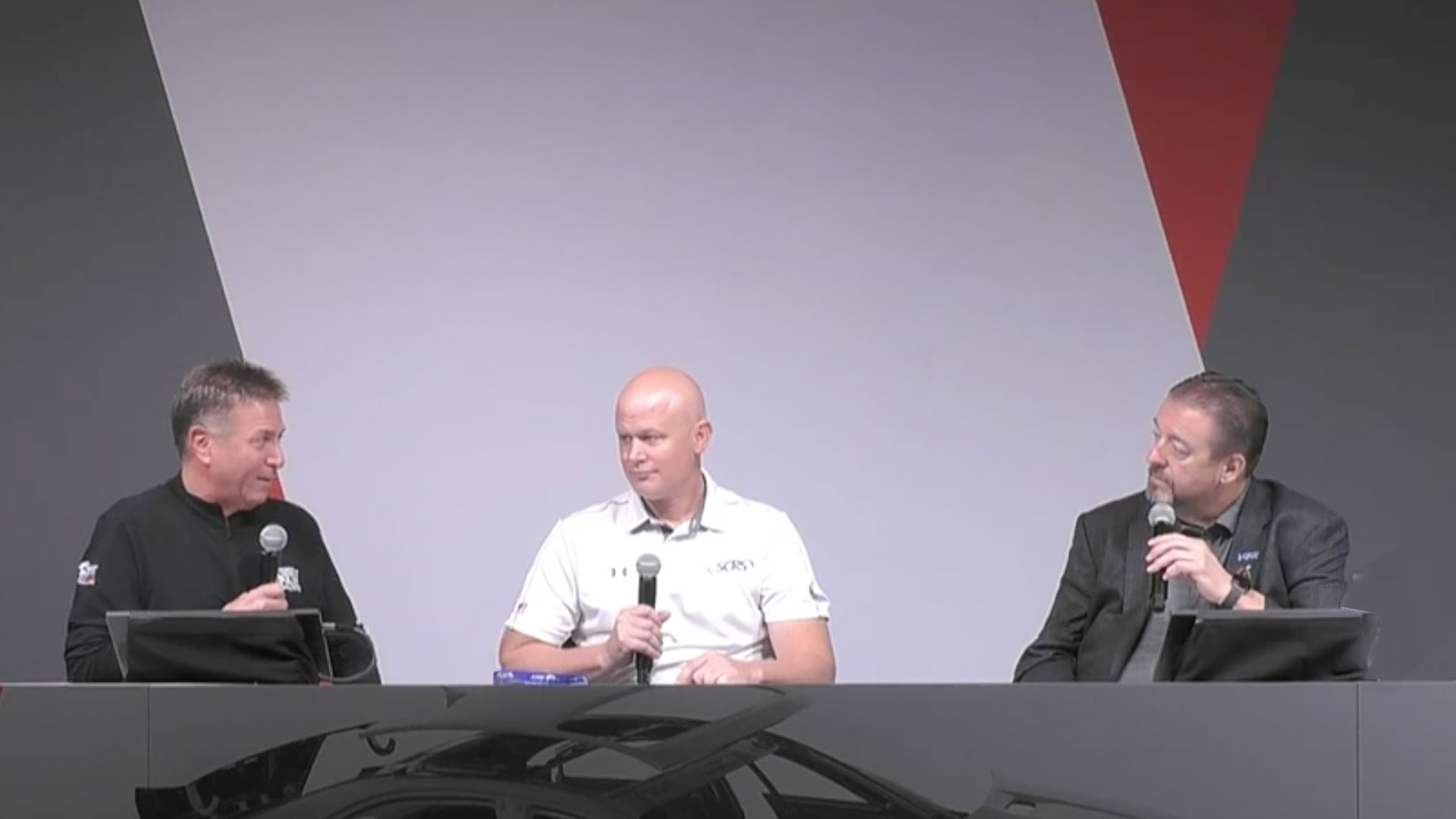 Three men seated at a conference panel, speaking with microphones