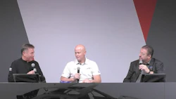 Three men seated at a conference panel, speaking with microphones