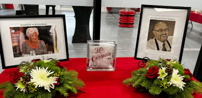 Memorial display with framed photos, red roses, white flowers, and a 'Let's Celebrate' candle