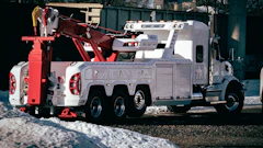 White and red heavy-duty tow truck parked on snowy ground near trees