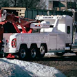 White and red heavy-duty tow truck parked on snowy ground near trees
