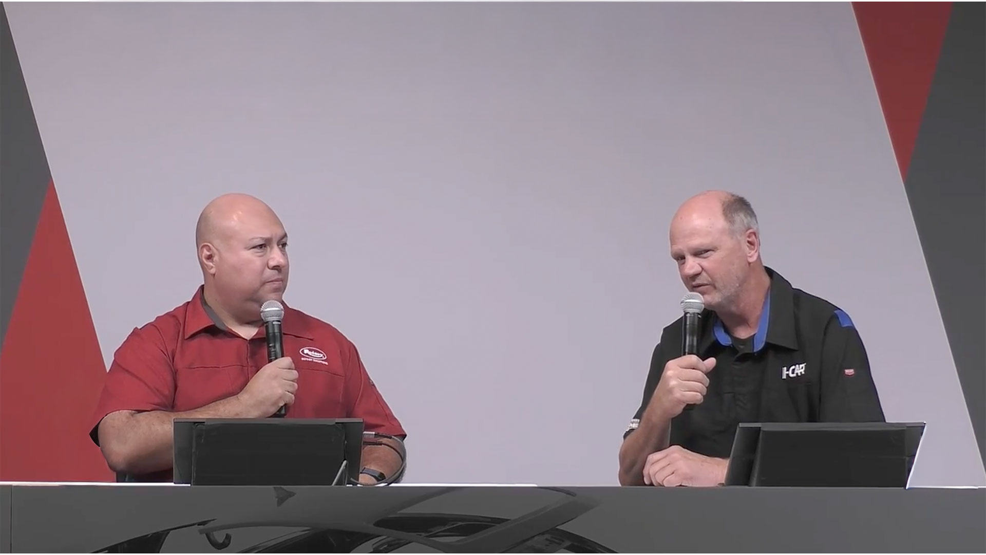 Two presenters speaking at a conference with microphones and dark background