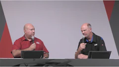 Two presenters speaking at a conference with microphones and dark background