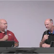 Two presenters speaking at a conference with microphones and dark background