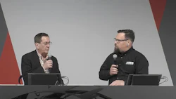 Two presenters speaking at a conference with microphones and computers