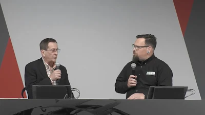 Two presenters speaking at a conference with microphones and computers