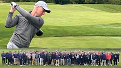 Golfer in gray outfit swinging club with large group posing on green golf course